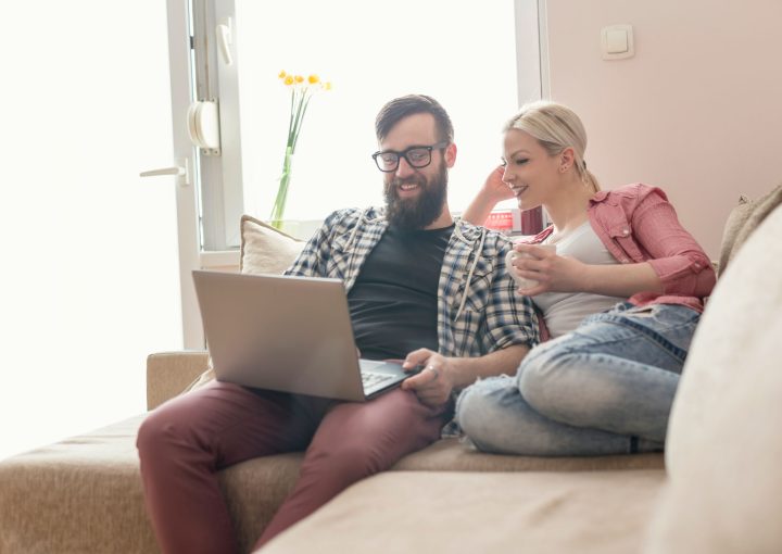 young couple smiling looking at laptop checking home loan rates